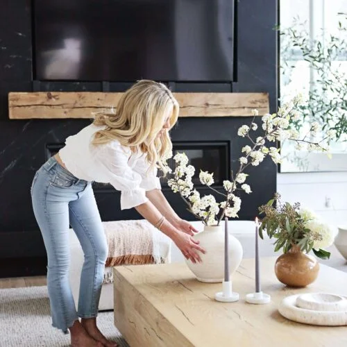 Woman arranging flowers in a vase on a coffee table.