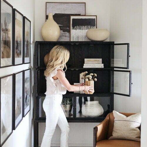 Woman in white jeans styling a bookcase.