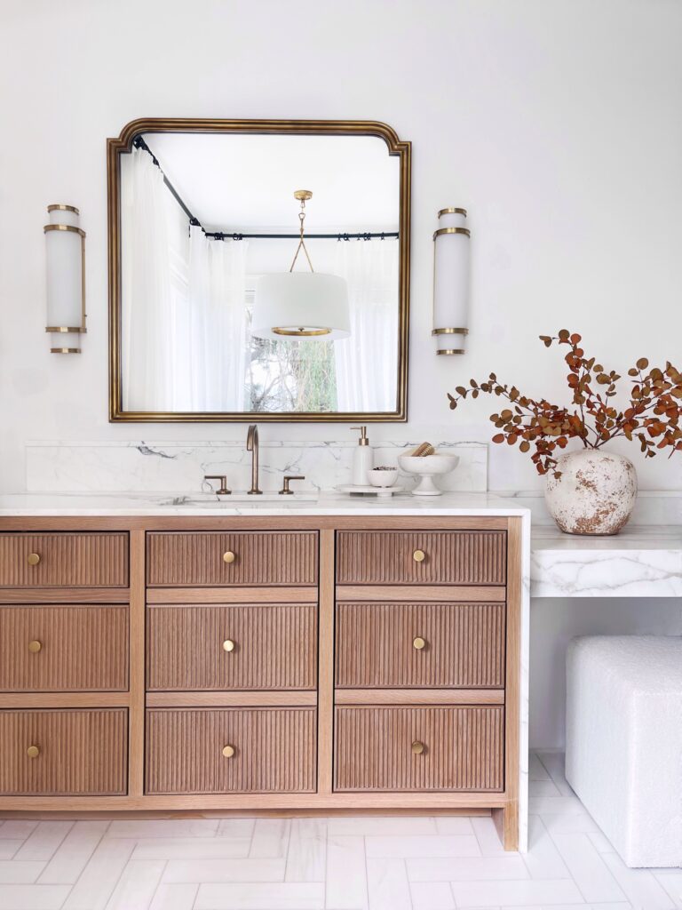 Bathroom vanity with gold accents and wood drawers.