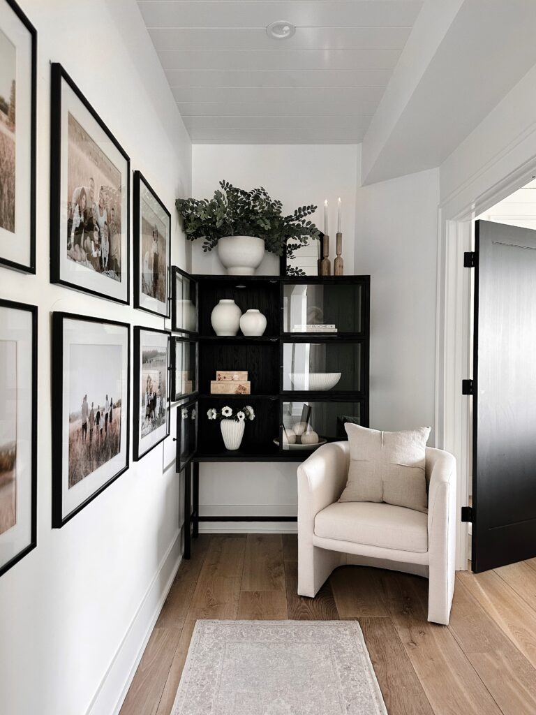 White chair with black bookcase and framed photos.