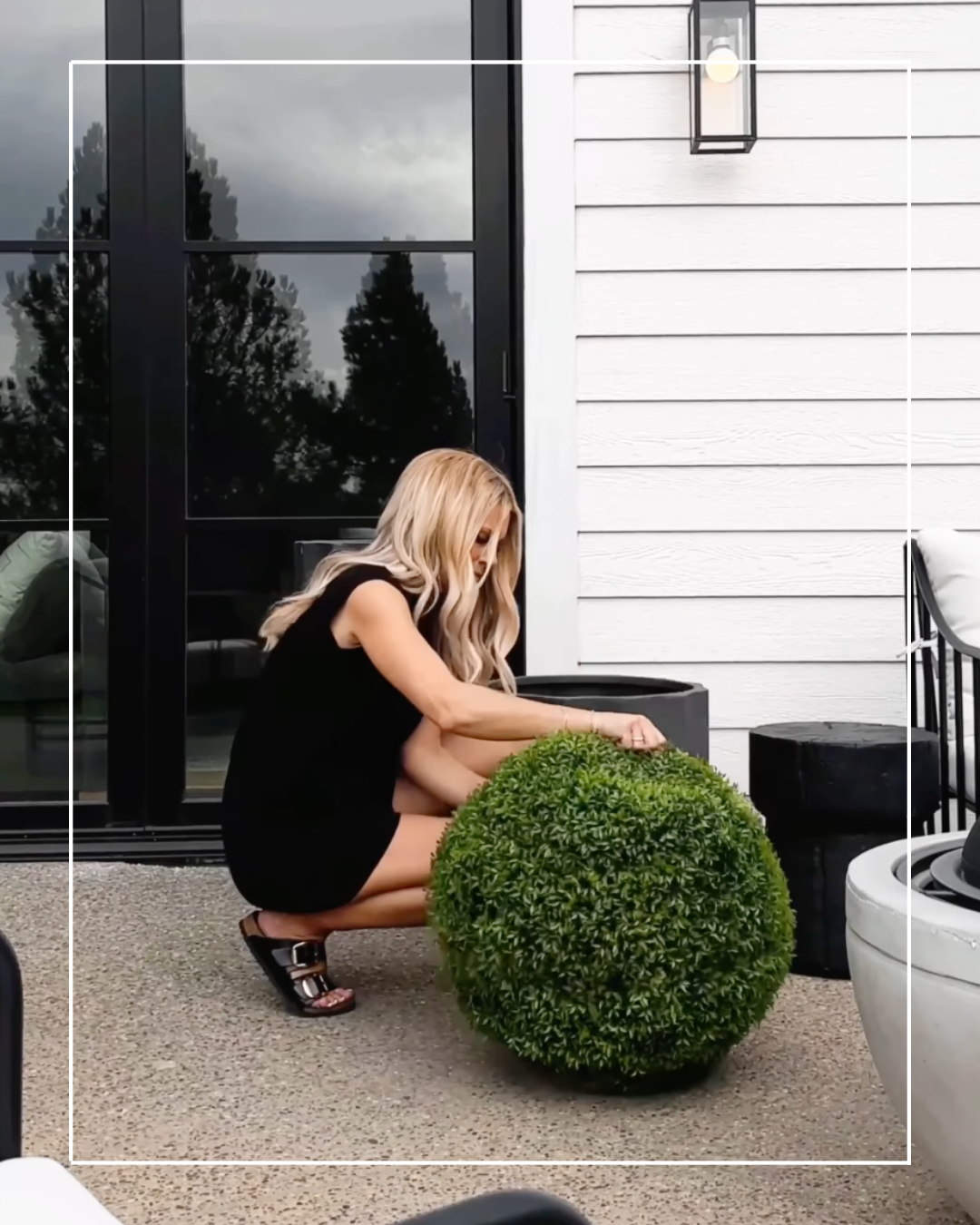 Woman in black dress next to topiary sphere.