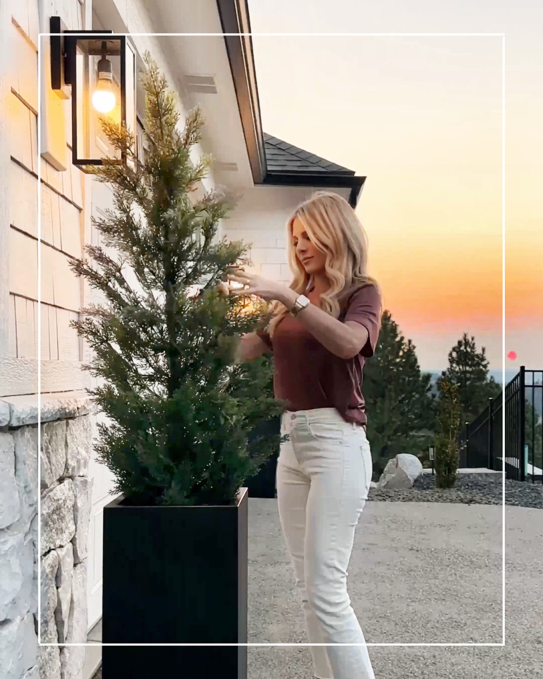 Woman decorating a potted tree outside a house.