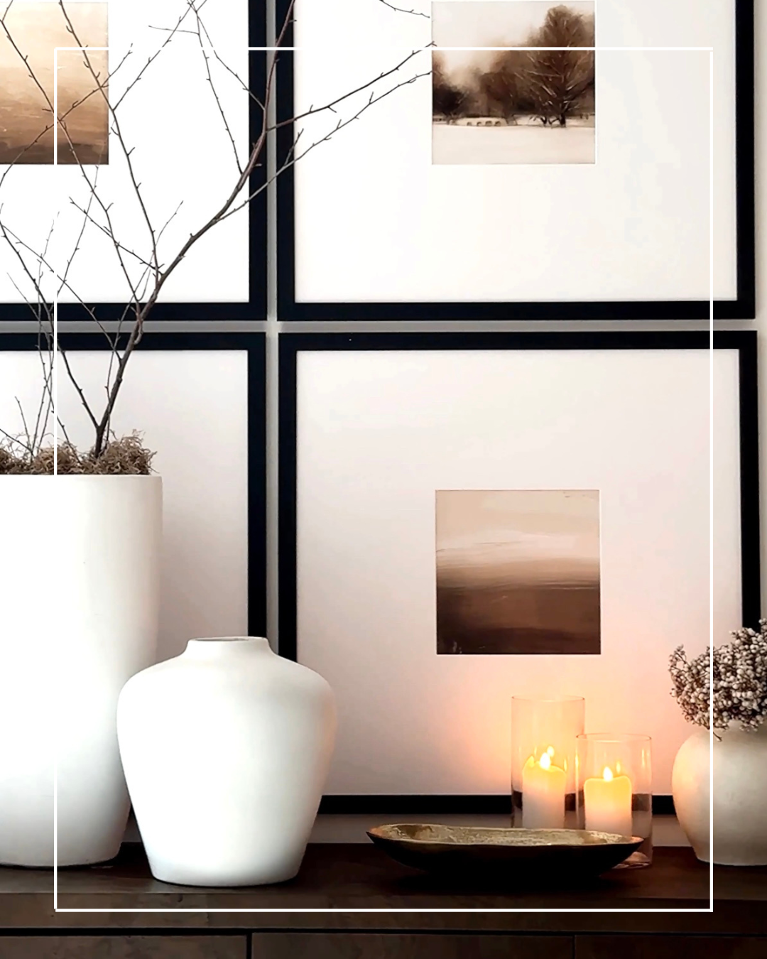 White vases, candles, and framed artwork on a table.