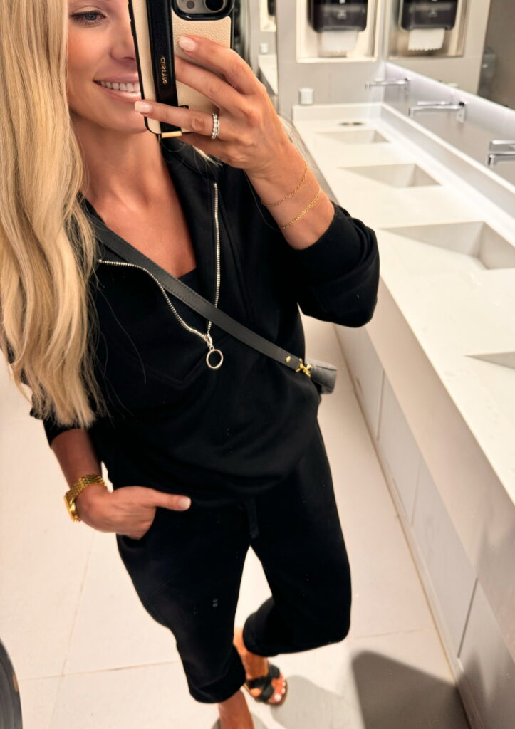 Woman in black outfit taking selfie in bathroom.